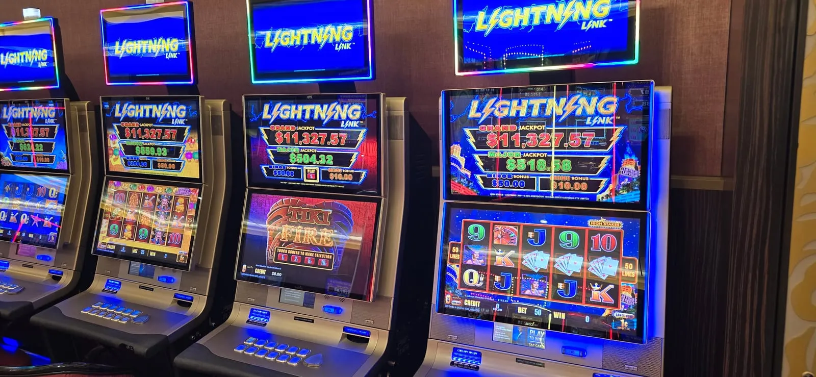 Four Lightning Link slot machines side by side, each topped with a blue Lightning Link sign, all displaying the same Grand jackpot of $11,327.57 but different Major jackpot values.
