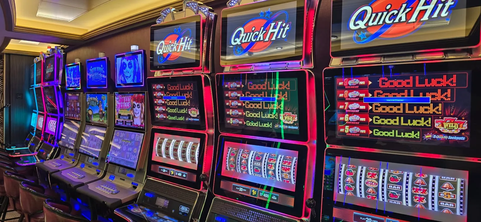 A curved bank of Quick Hit slot machines, each with a lit Quick Hit topper above a screen reading 'Good Luck!' beside the Quick Hit jackpot ladder, with more cabinets receding down the row.