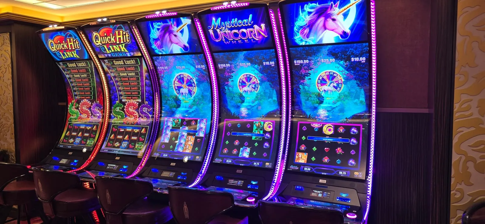 Quick Hit Link and Quick Hit Link Gems cabinets beside three Mystical Unicorn Wheel machines with purple unicorn artwork and a bonus wheel on each upper screen.